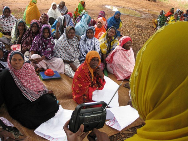 The image shows a group of women listining to a local radio broadcast.